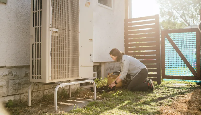 Heat pump installed outside of home with homeowner gardening