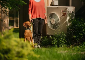 A women standing next to her heat pump with a cute dog
