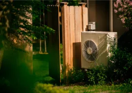A heat pump outside of a home with a lush garden